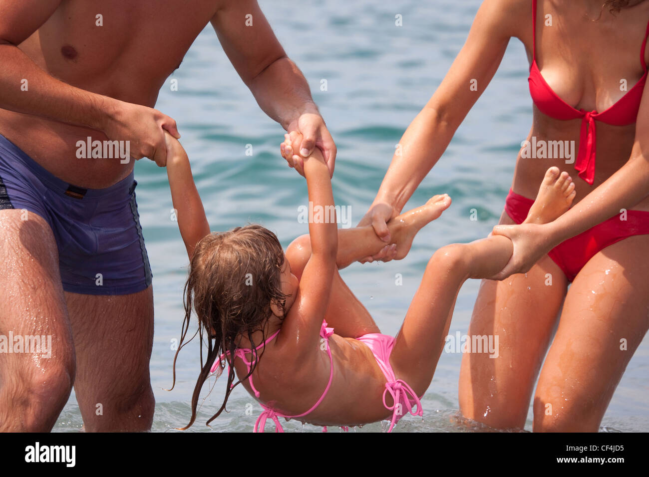 young family bathes in sea. wet happy daddy and mum play with daughter  standing in water Stock Photo - Alamy