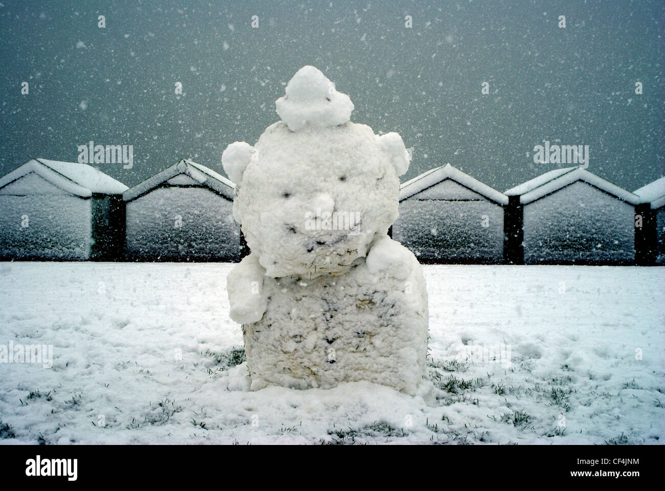 A snowman on Hove Lawns with snow covered beach huts in the background. Stock Photo
