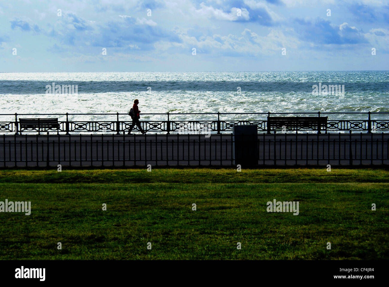 A lone figure walking along Hove promenade with the sea in the background. Stock Photo
