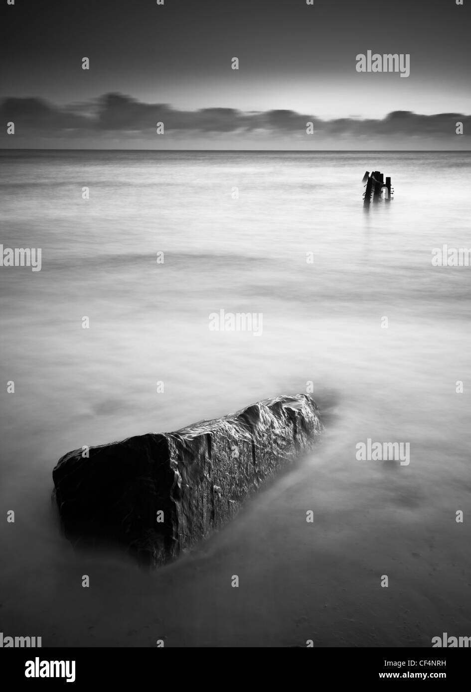 A single rock in the sea points in the direction of a lost jetty on the north-east coast of Norfolk. Stock Photo