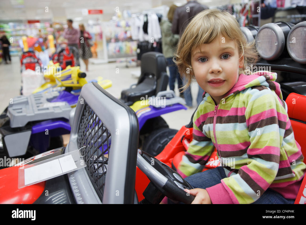 little girl in supermarket alone, chooses in department of toys. sits in an electromobile Stock Photo