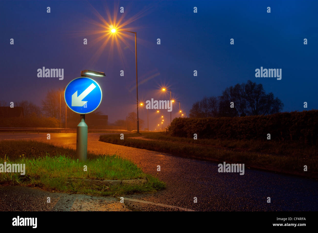 A road sign indicating to keep left, lit up at dusk. Stock Photo