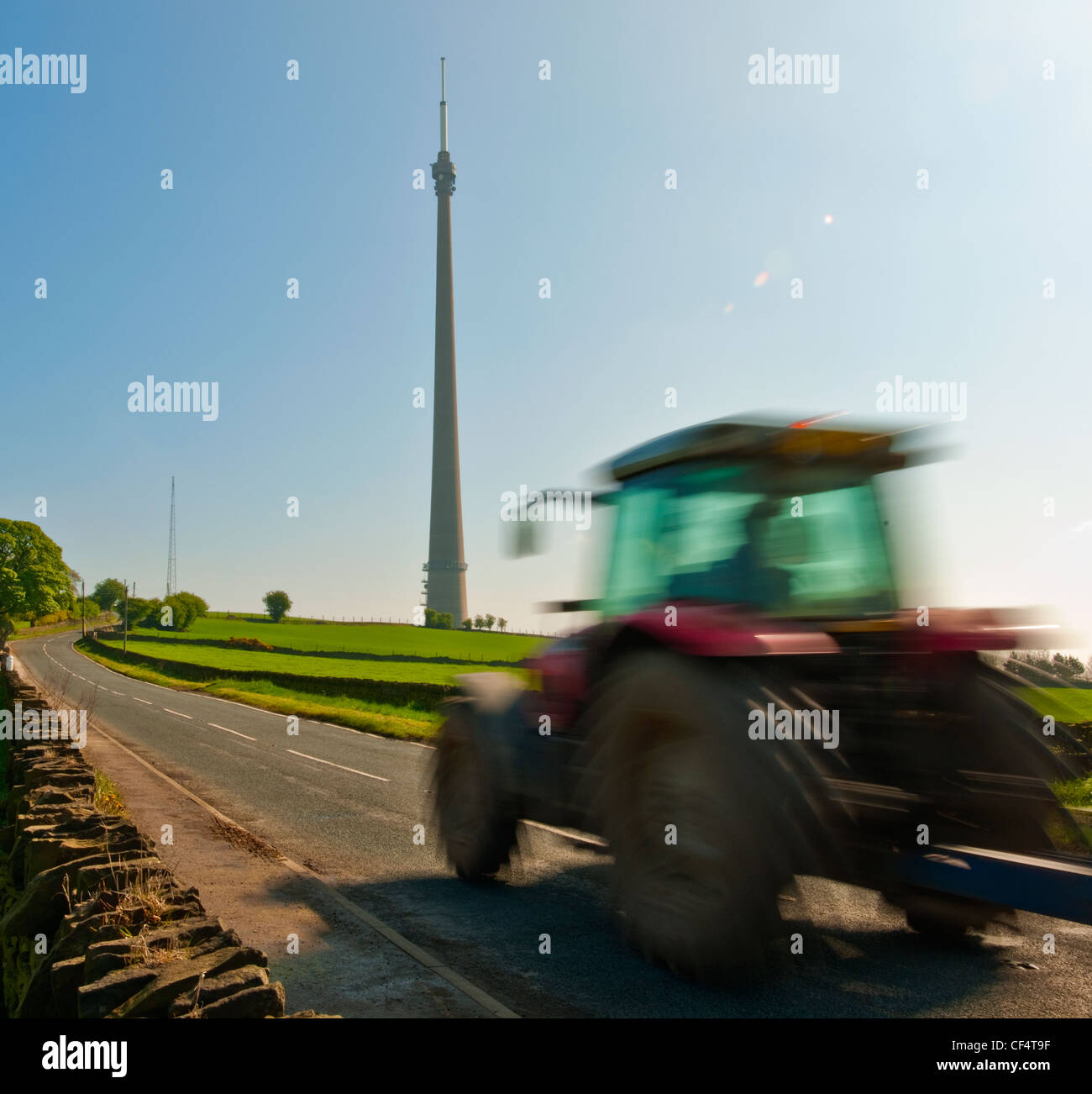A tractor travelling along a road on Emley Moor past the Emley Moor Tower, a television transmission tower which is the tallest Stock Photo