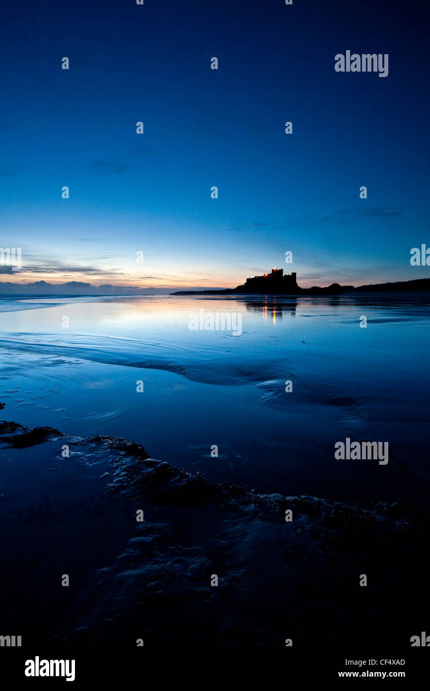 Lights from Bamburgh Castle reflecting in the low tide just before dawn. Stock Photo