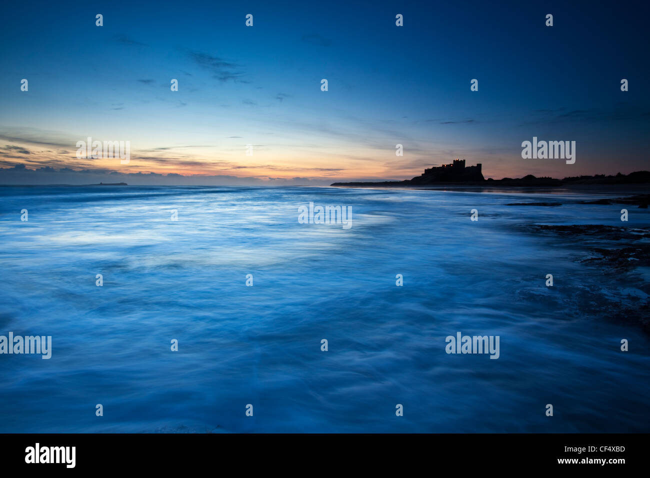 View across the shore towards Bamburgh Castle silhouetted by early dawn light. Stock Photo