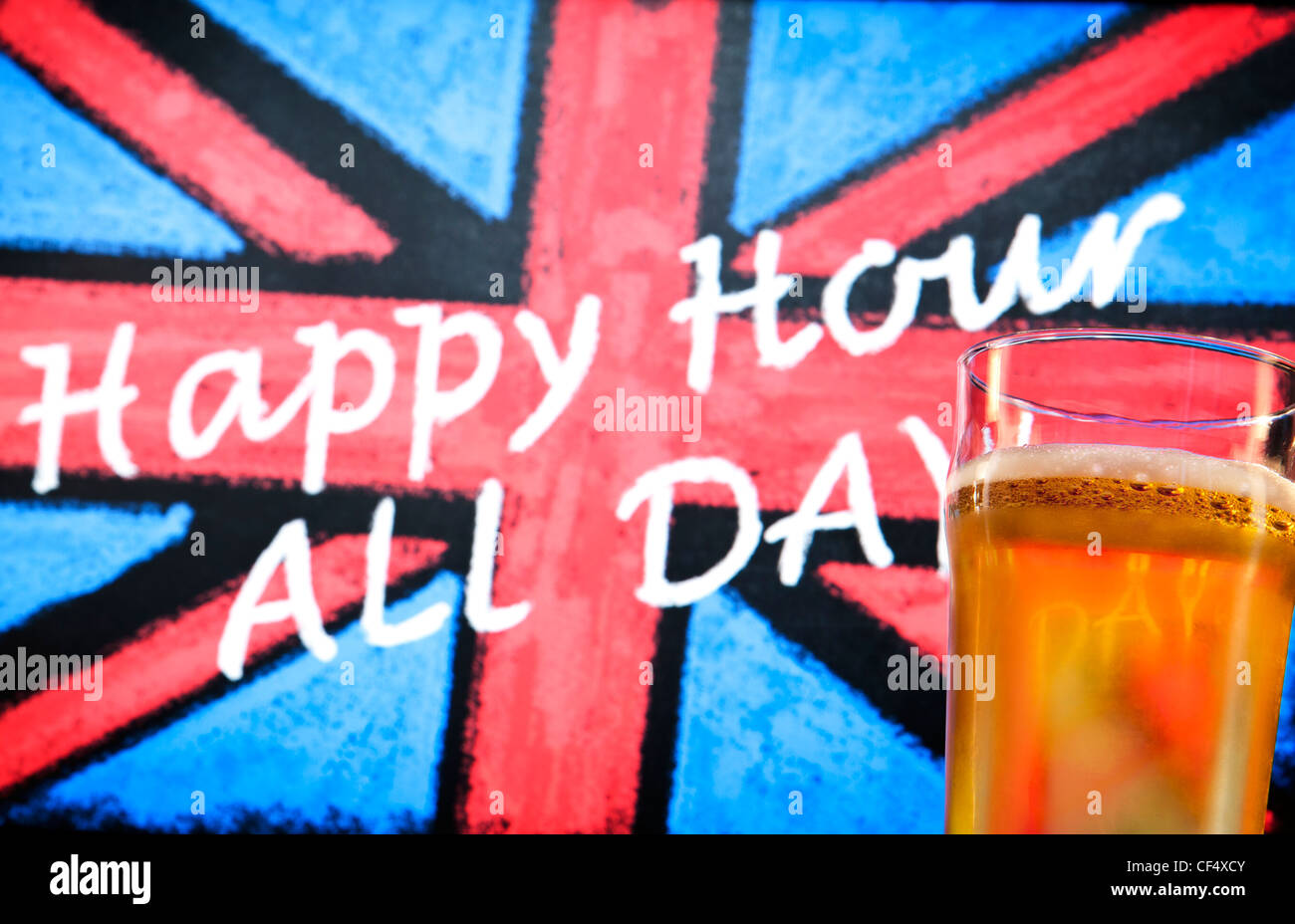 Blackboard pub sign with a chalk drawn Union Jack, which reads 'Happy Hour All Day' and a pint glass of beer in the foreground Stock Photo