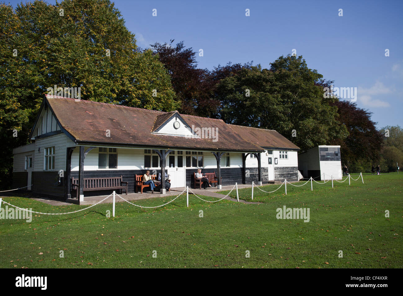 people sitting on wooden benches in front of Bakewell cricket pavilion Derbyshire East Midlands England Stock Photo