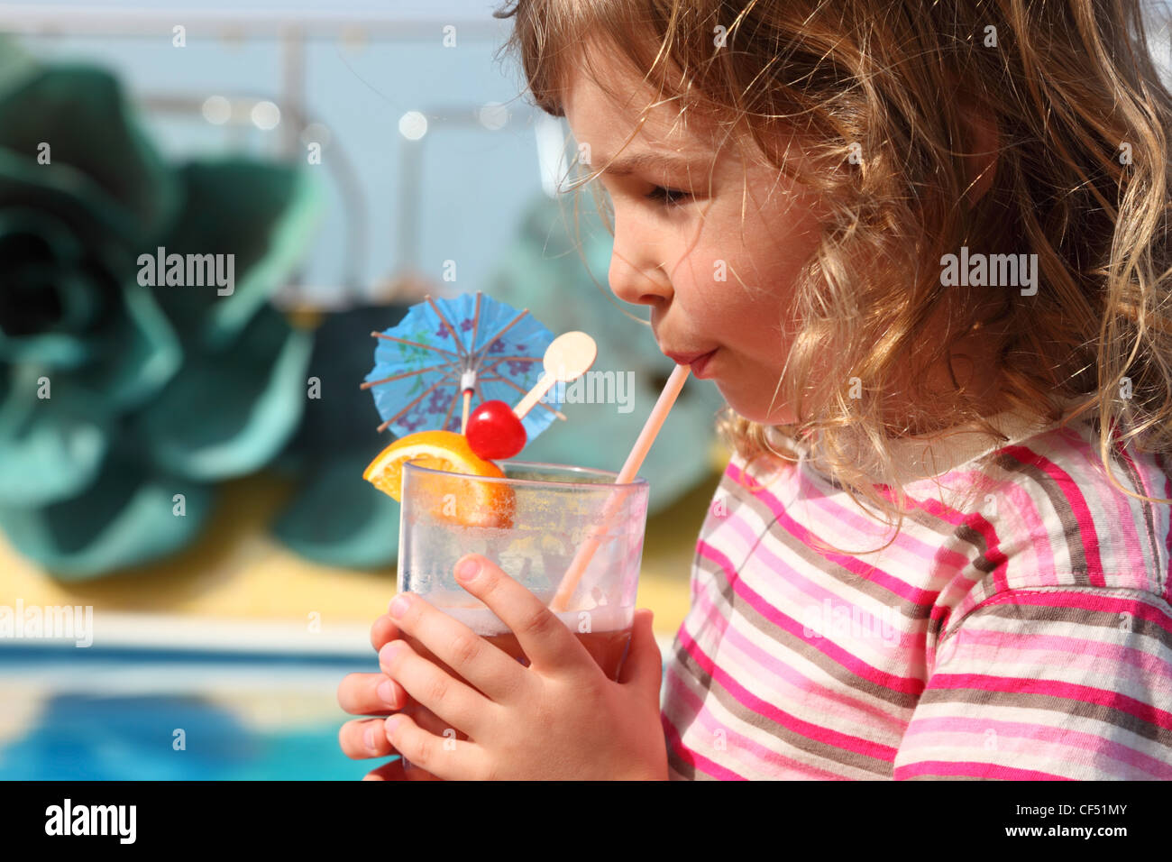 little girl in shirt with pink stripes drinking cocktail with fruits, side view Stock Photo