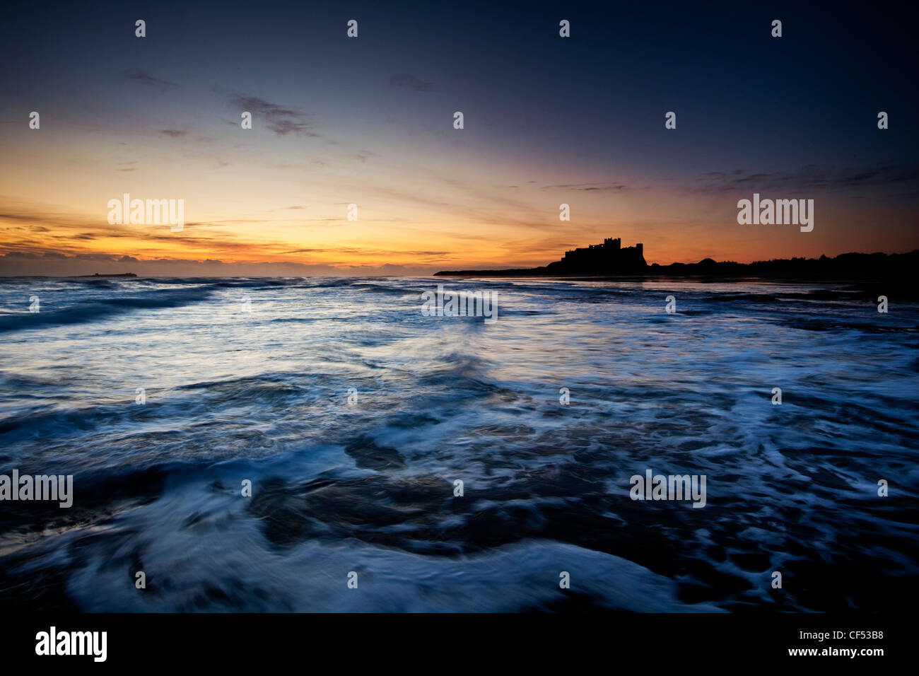 Waves rolling onto the beach by Bamburgh Castle at dawn. Stock Photo