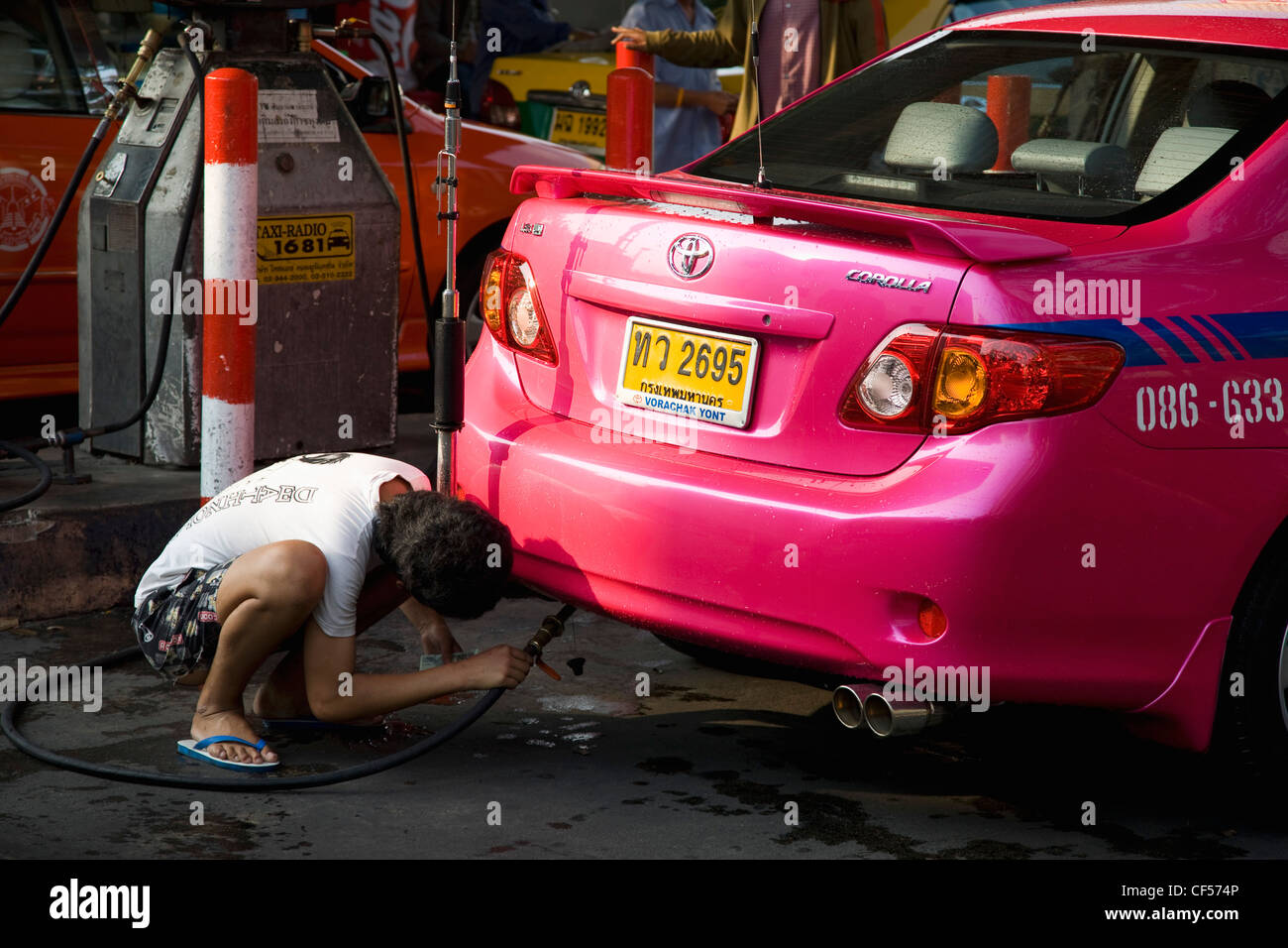 Thailand, Bangkok, Pink metered taxi cab being refuelled with LPG gas pipe at filling station by male driver. Stock Photo