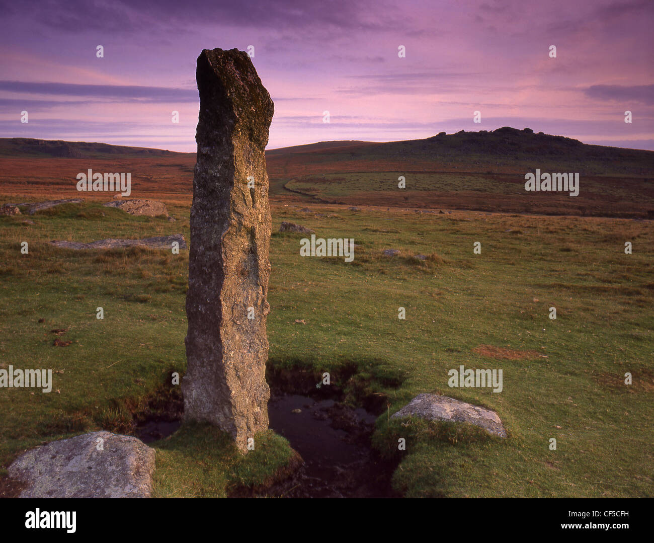 View of single standing stone in moorland with small tor on the horizon ...
