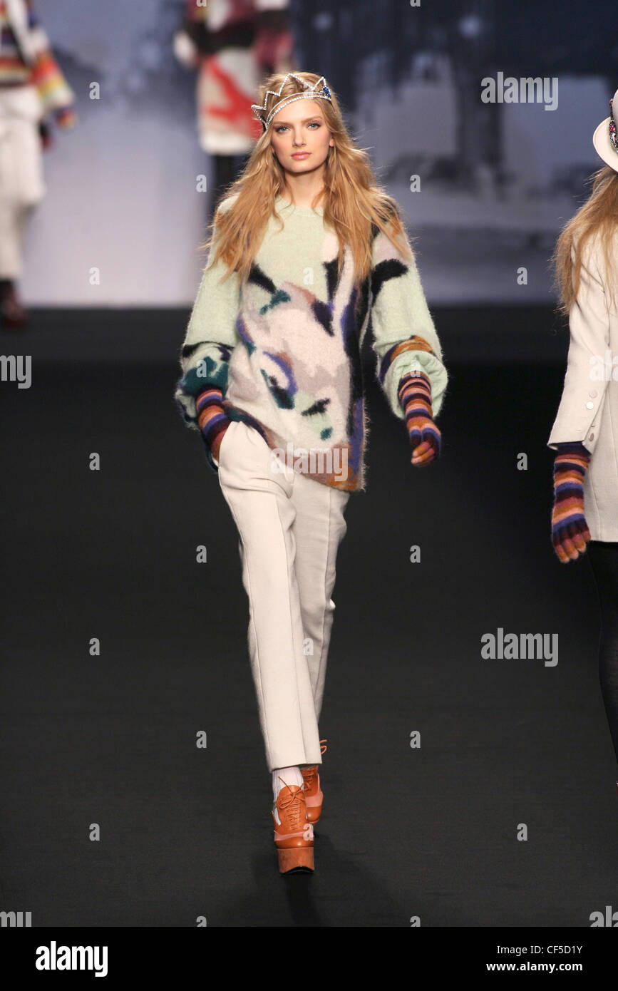 Female wearing a multi coloured mohair jumper cropped bell sleeves, white cropped trousrs and long striped multi coloured Stock Photo