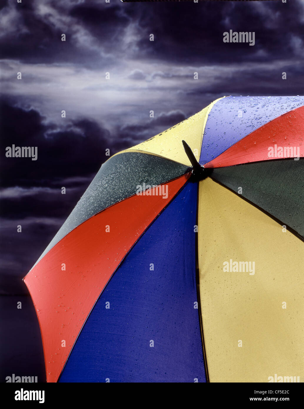 Multi coloured large umbrella with raindrops on its surface with storm