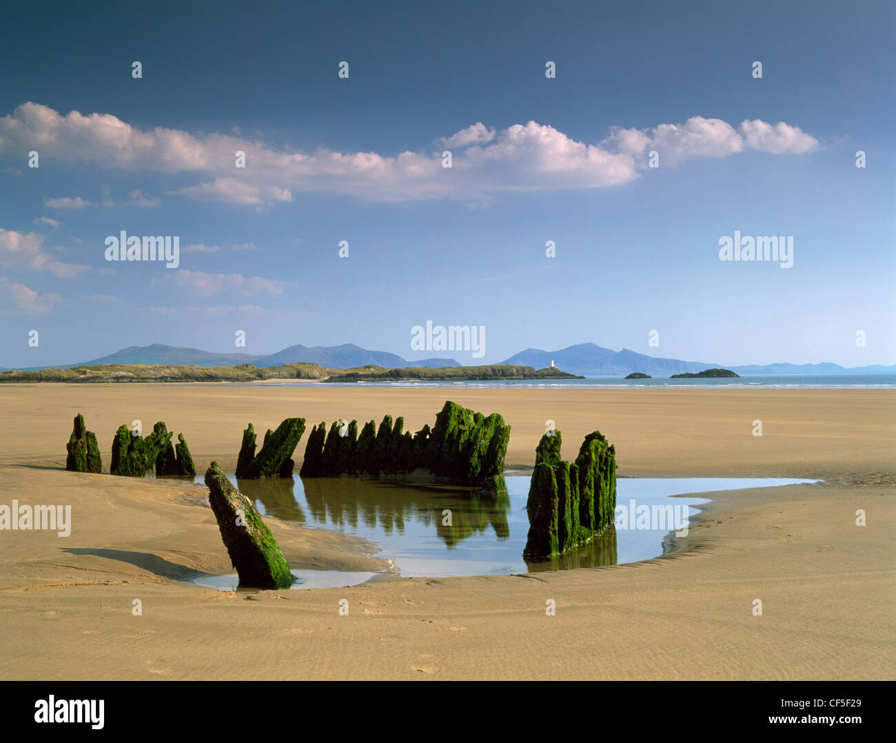 A shipwreck trapped in the sands of Traeth Penrhos, with Llanddwyn Island and the peaks of Snowdonia and Lleyn beyond. Stock Photo