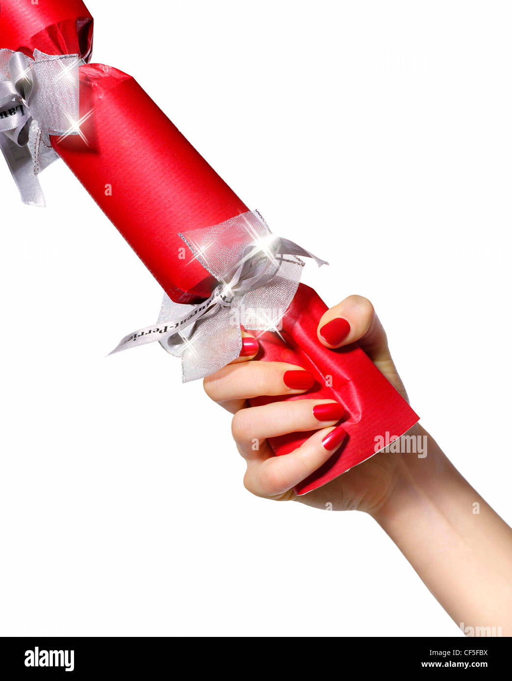 Female wearing bright red nail varnish pulling a red Christmas cracker with silver ribbon Stock Photo
