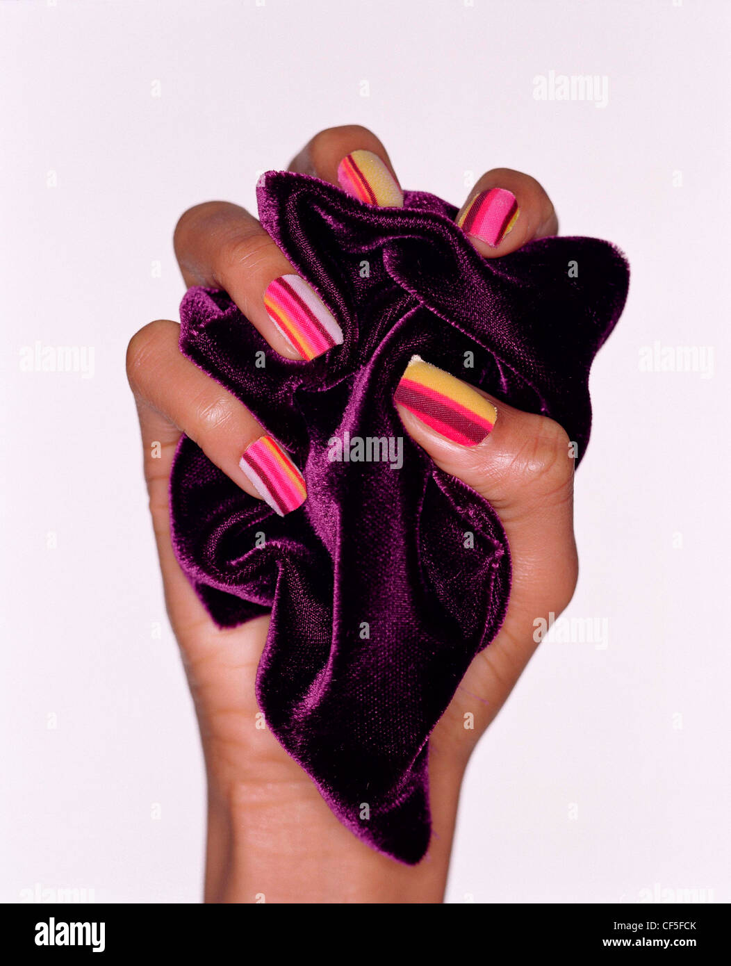 Female wearing pink striped nail varnish holding a piece of purple fabric in her fist Stock Photo