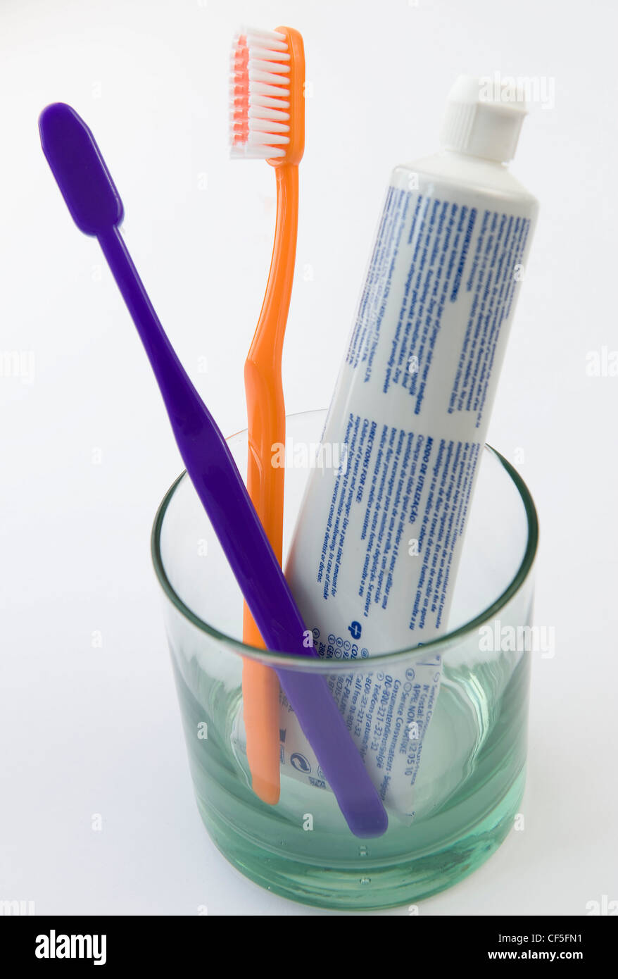 A clear glass with tube of toothpaste, a purple toothbrush and yellow