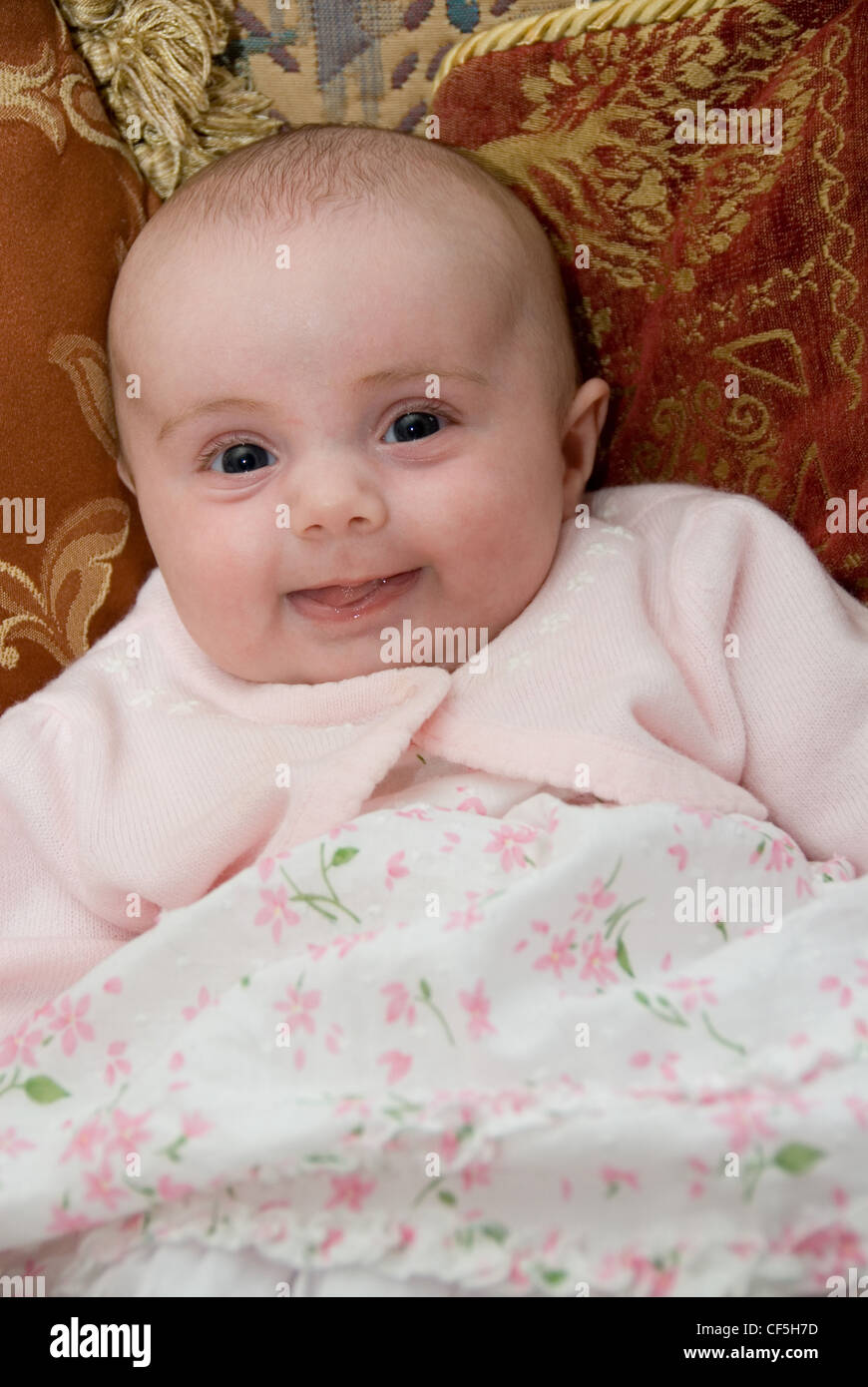 A three month old female dressed in white dress pink flowers and a pale