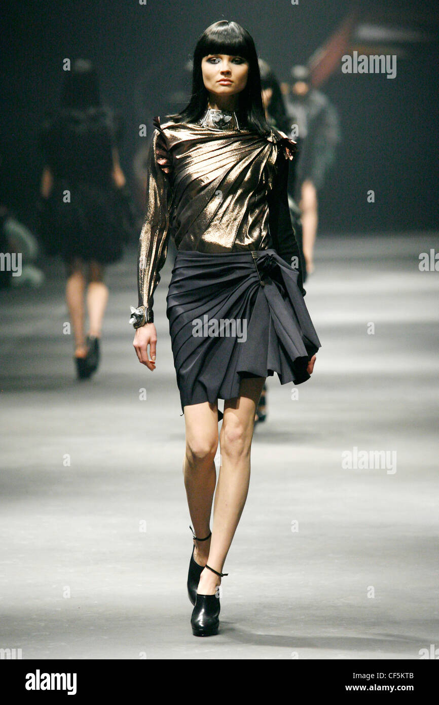 Lanvin Paris Ready to Wear Autumn Winter A model wearing a gold lame long sleeved top a funnel neck, and gathering pleated Stock Photo