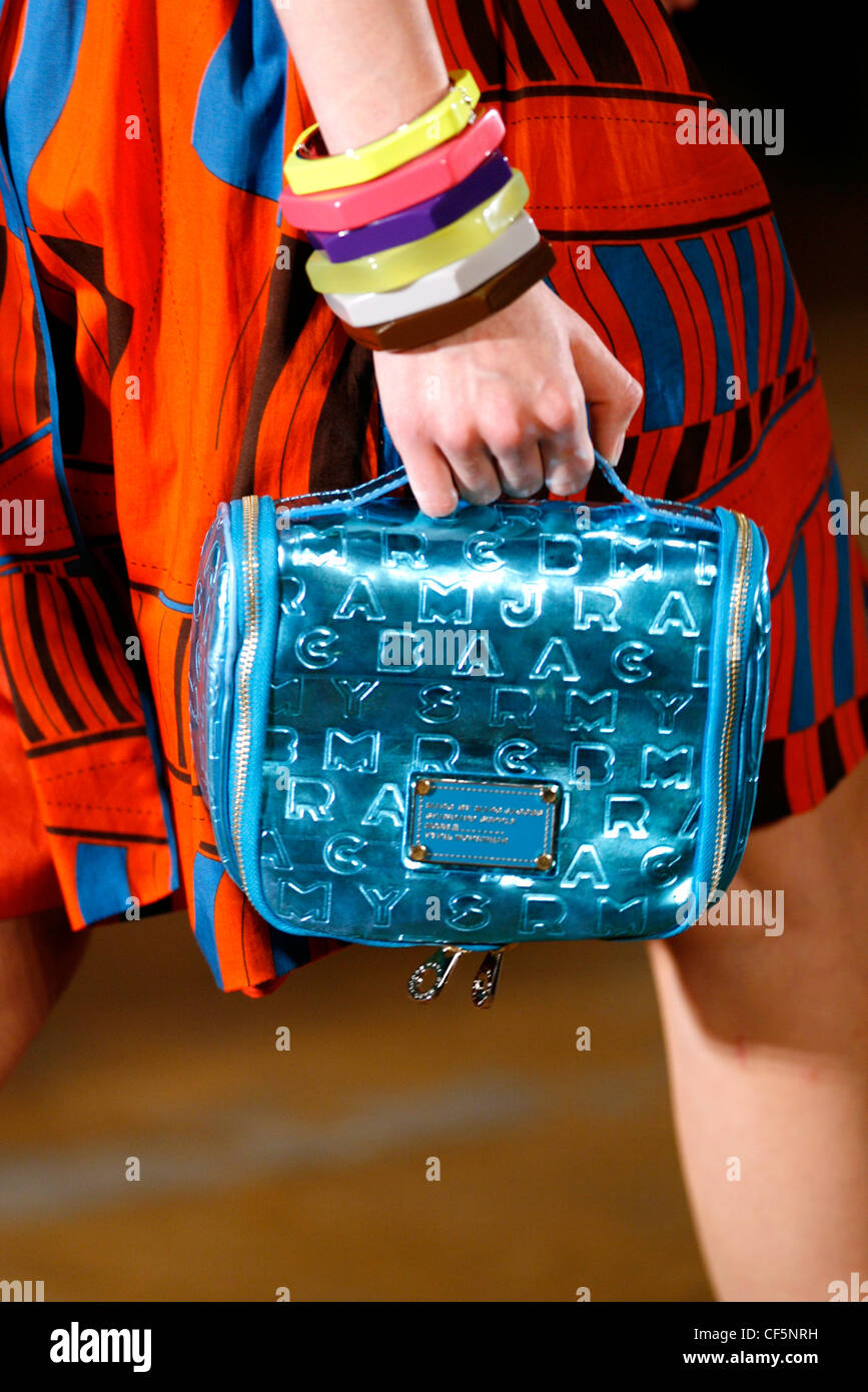 A close up of an orange, blue and brown patterned short sleeved a line dress, a metallic blue embossed handbag and multiple Stock Photo