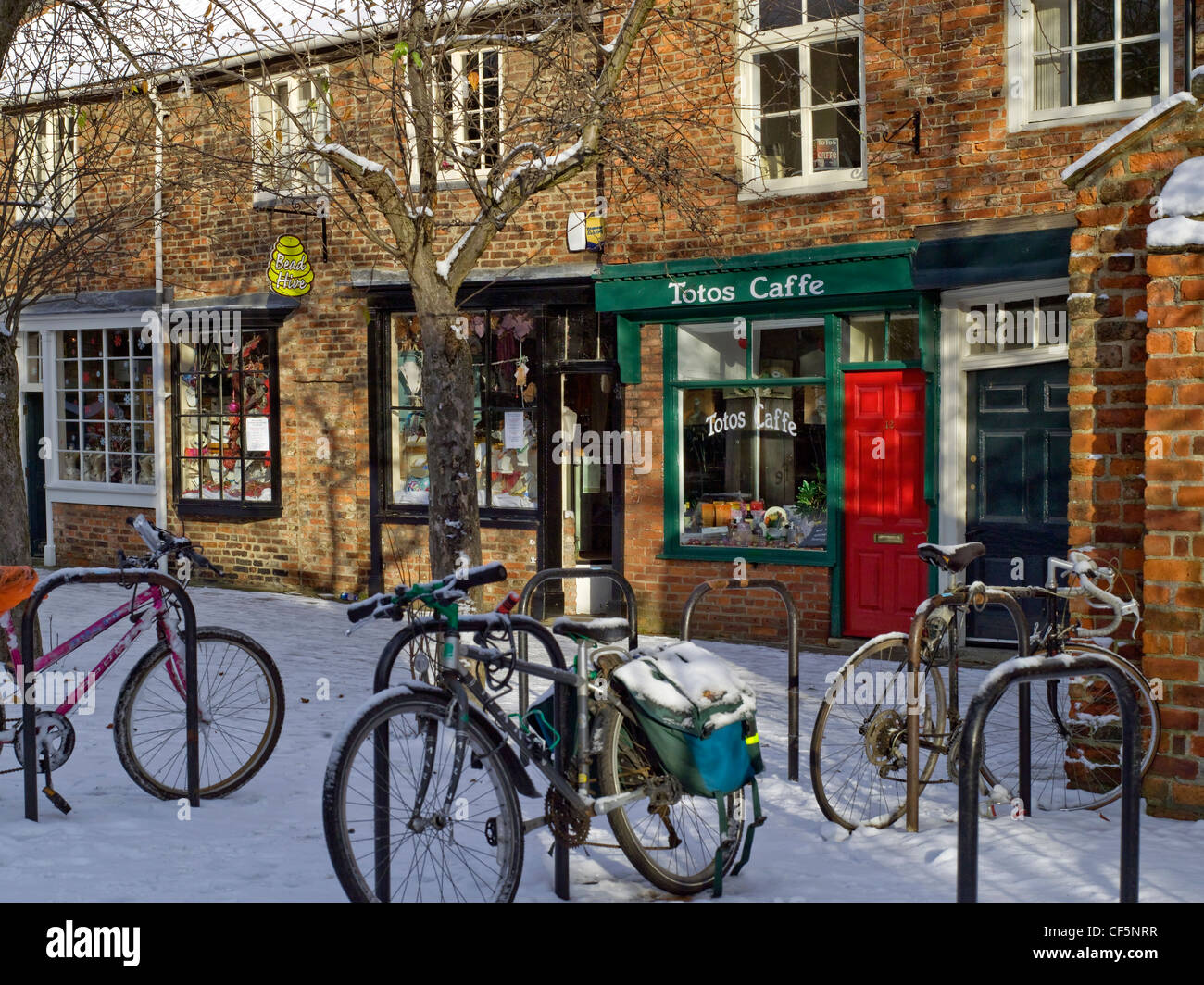 Bicycles locked to bike racks in the snow outside a row of shops in Minster Close. Stock Photo
