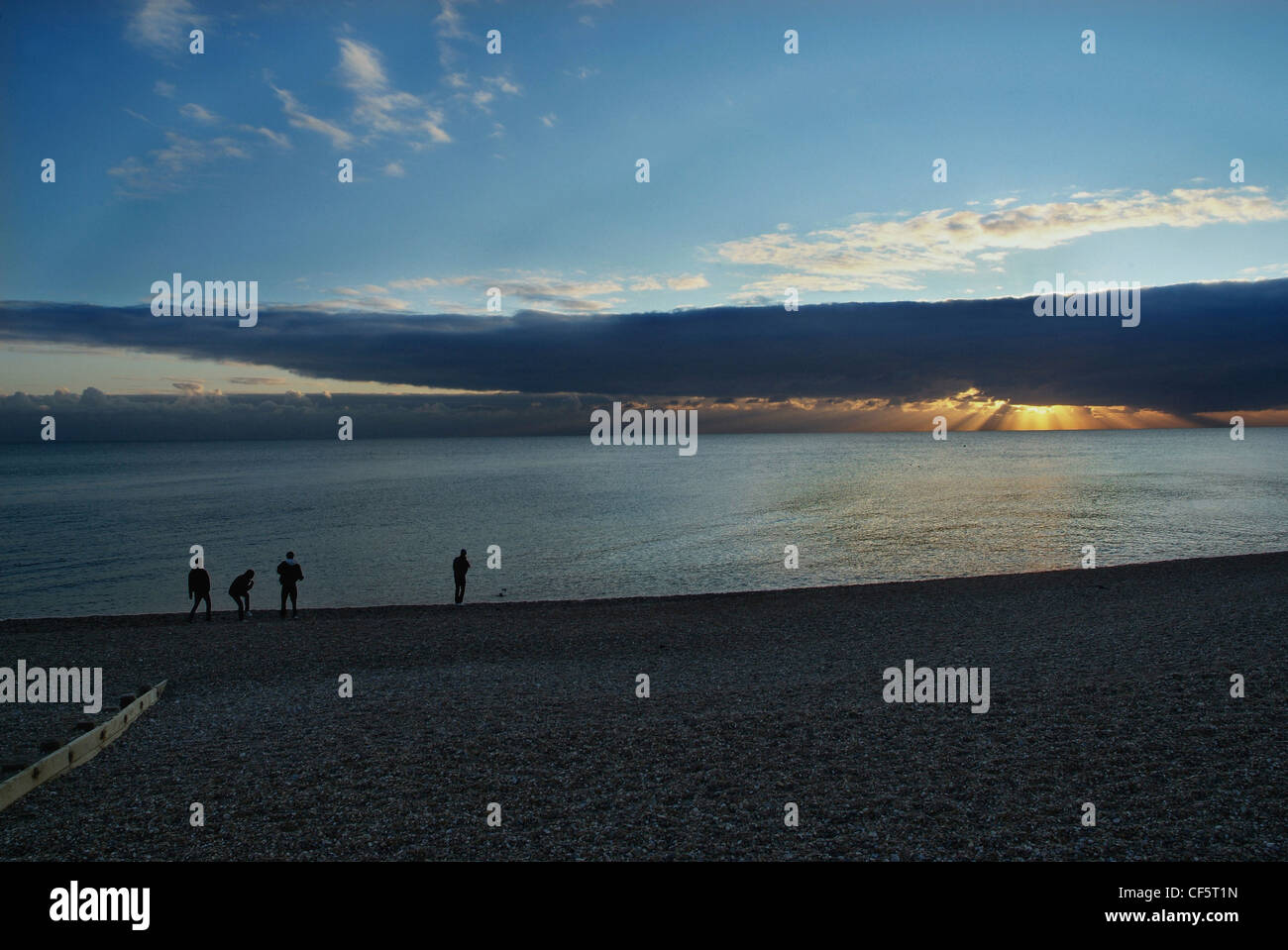 Young men skimming stones into the sea on Hove beach at sunset. Stock Photo