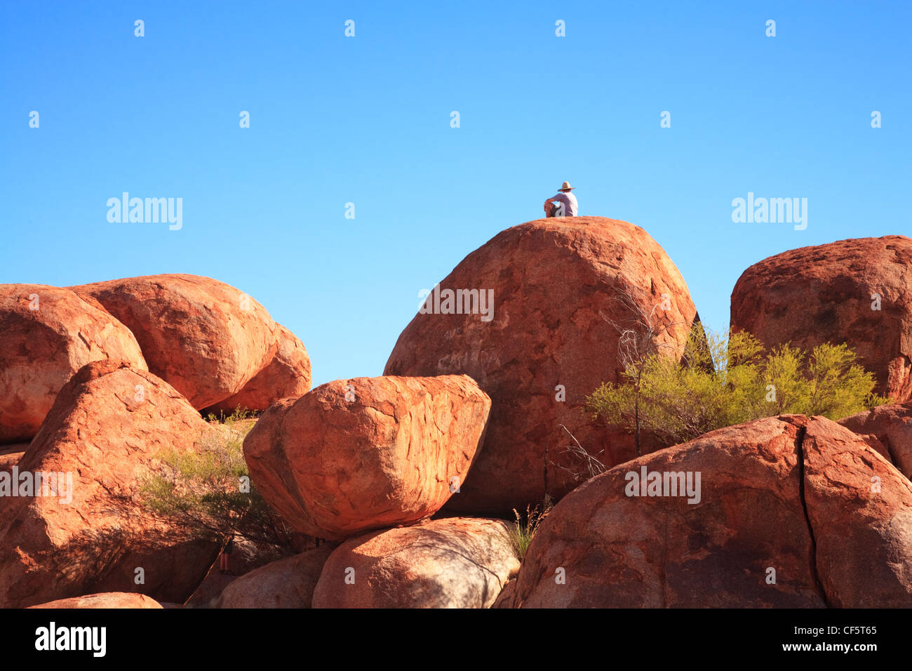 Devils Marbles, rock formations in the Northern Territory, Australia, with a man in a hat sitting on top. Stock Photo