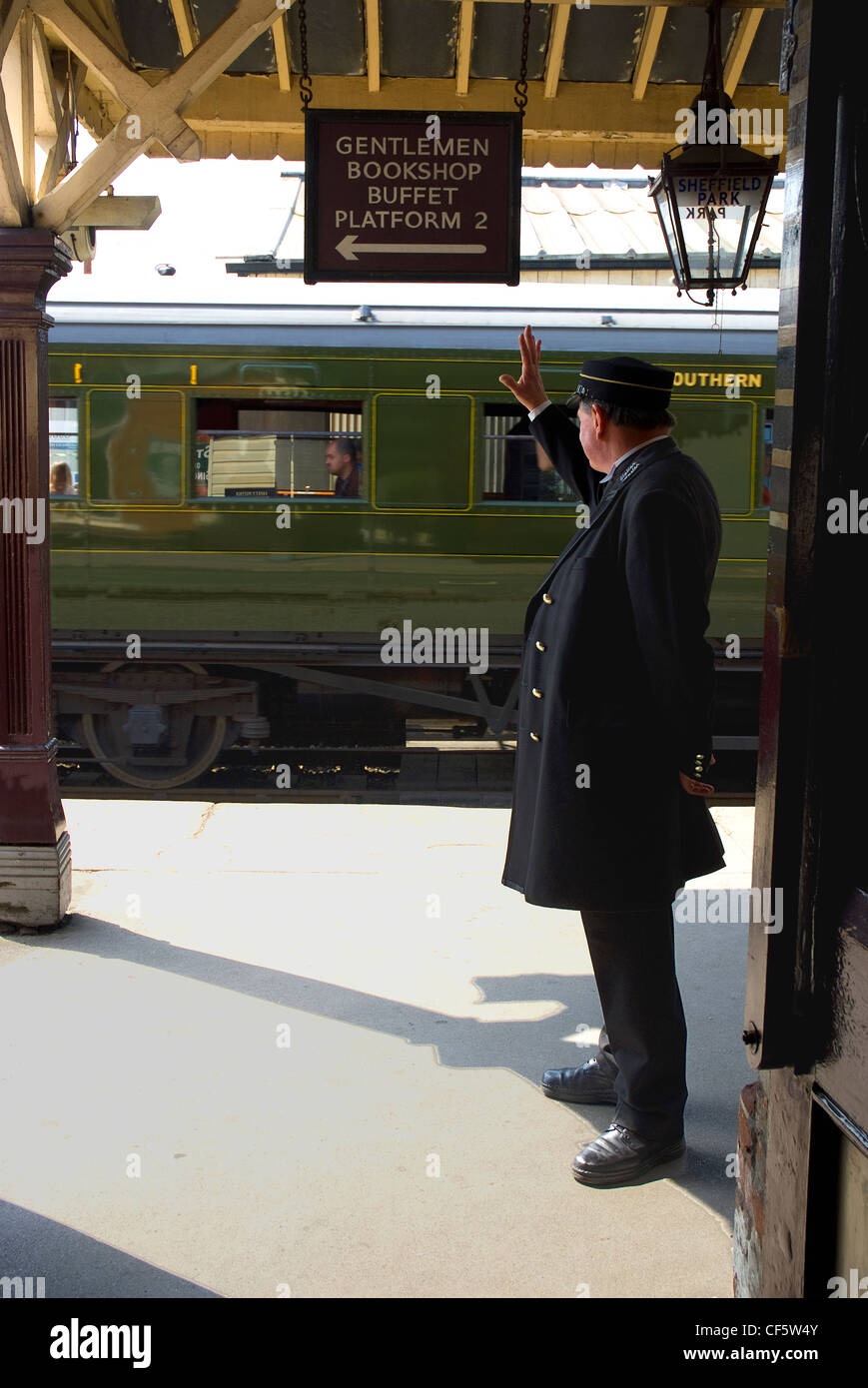 The Station Master waves a train off at Sheffield Park Station on the Bluebell Railway. Stock Photo