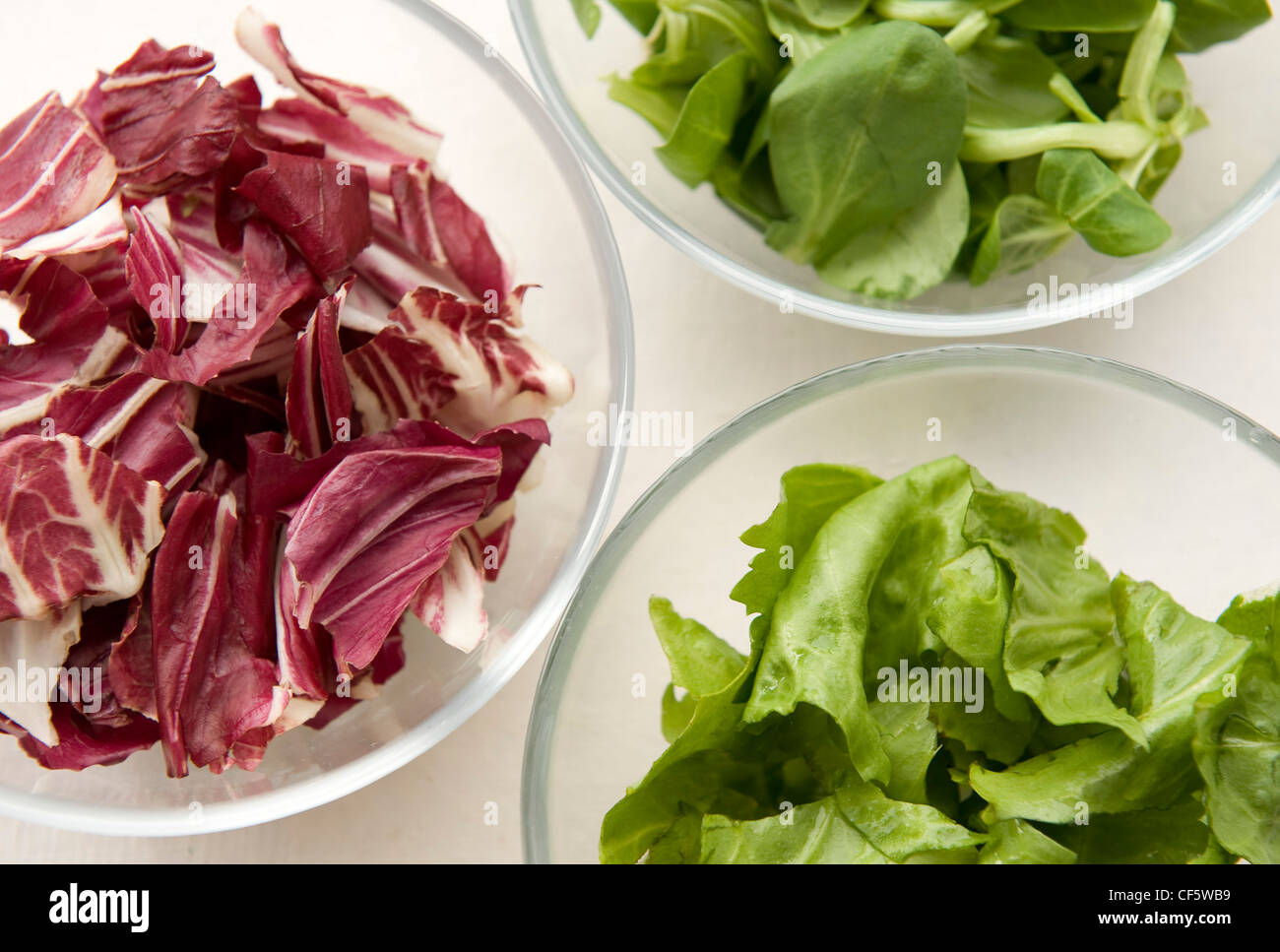 A still life image of three glass bowls with spinach leaves, green