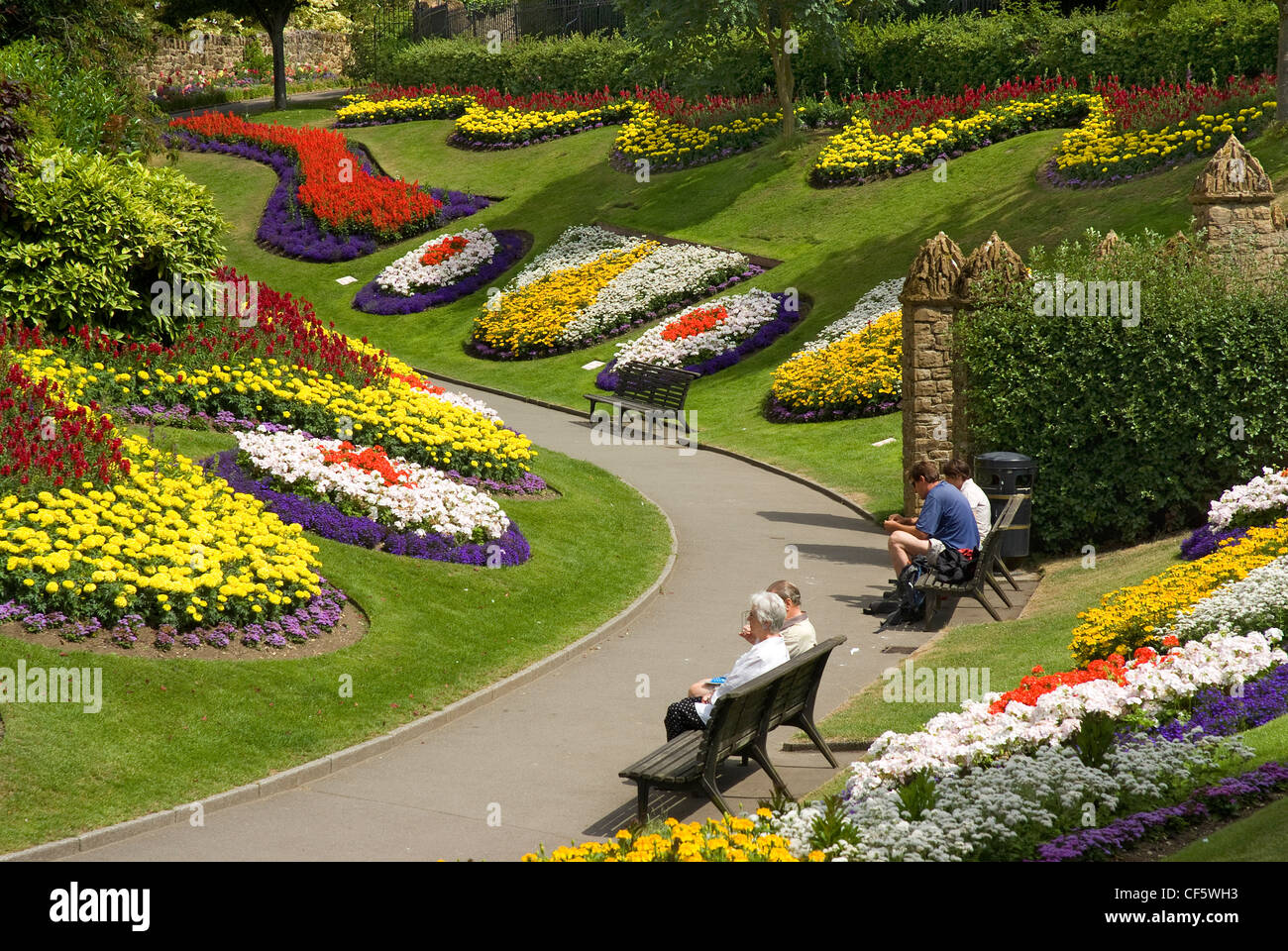 People sitting on benches amongst a stunning floral display in the grounds of Guildford Castle. Stock Photo