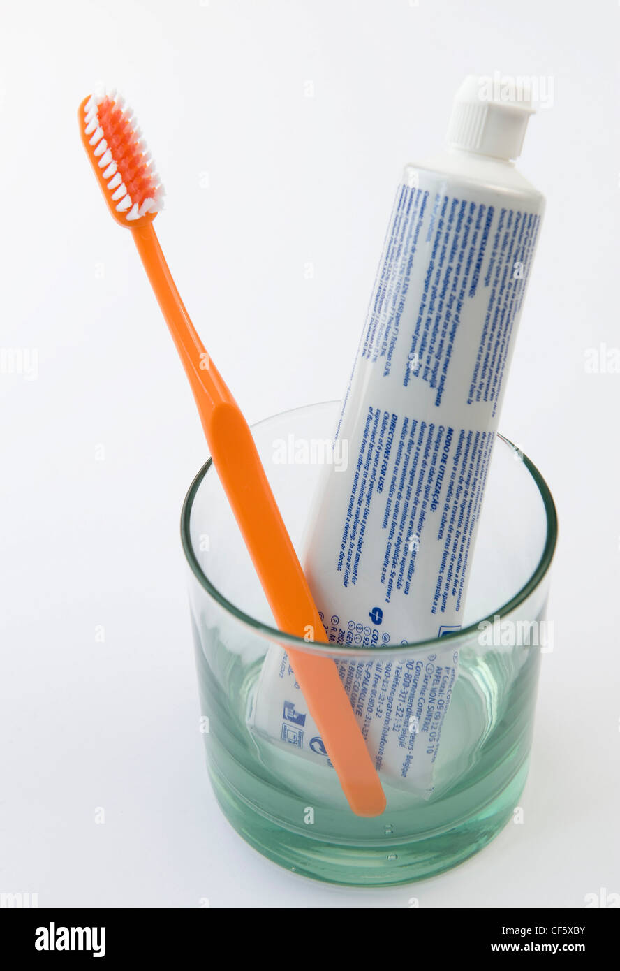 A clear glass with tube of toothpaste and yellow toothbrush in it Stock