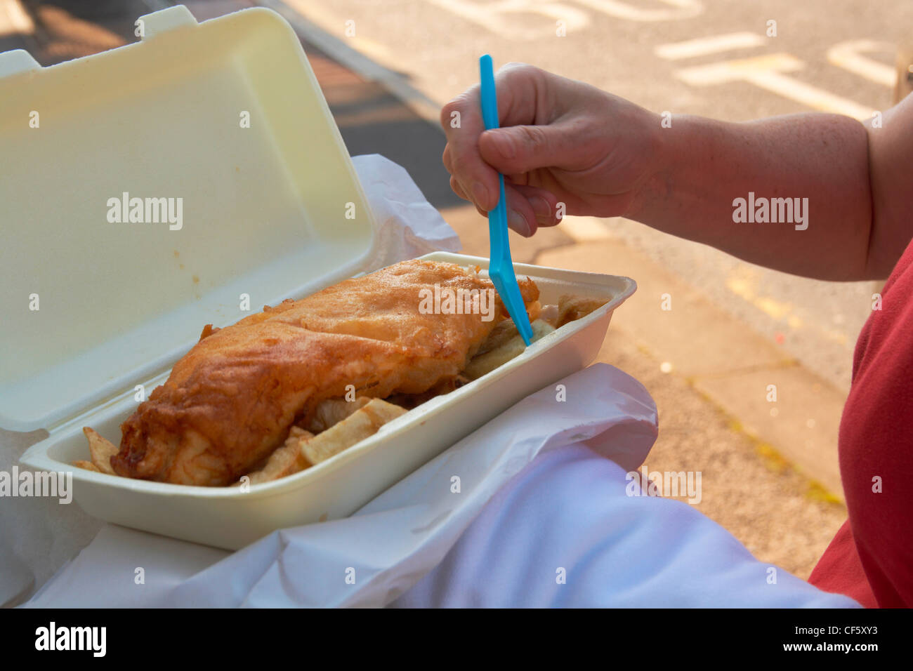 A close up of a woman eating fish and chips from a tray on Morecambe