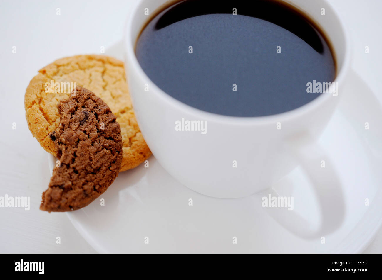 A white cup and saucer filled black coffee, a ginger biscuit and half a