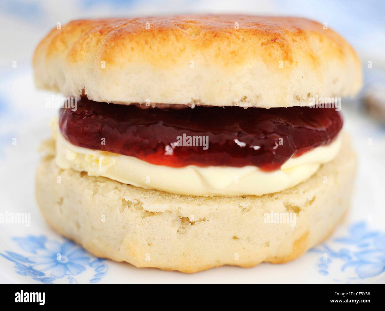 A close up of a scone filled with jam and clotted cream on a white ...