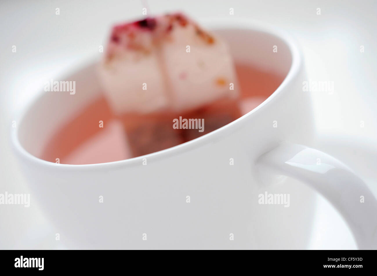 A close up of a white cup and saucer filled with a pink fruit tea with the tea bag still in it Stock Photo