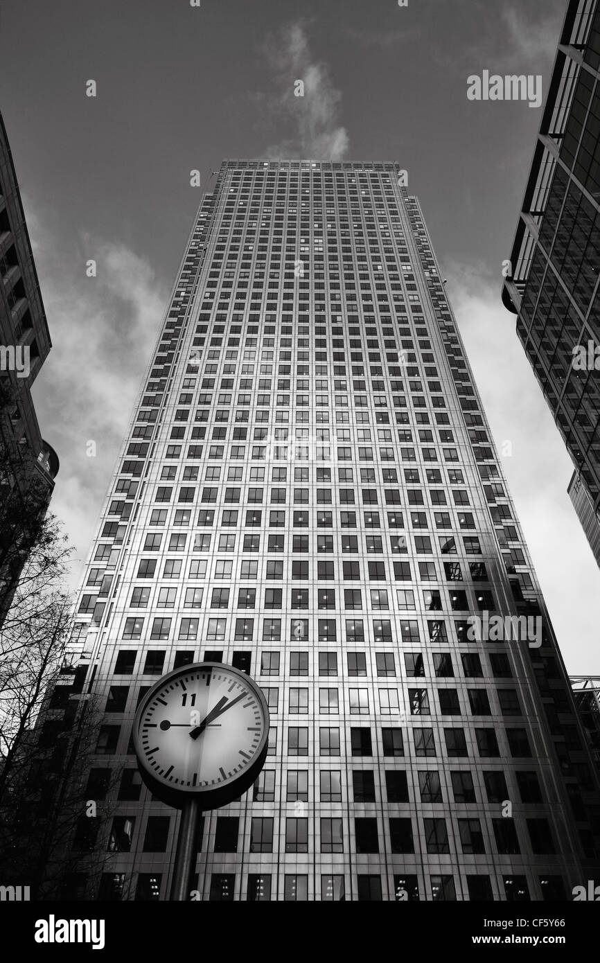 Looking up past a clock in Cabot Square to the Canary Wharf Tower (One Canada Square) the UK's tallest building. Stock Photo