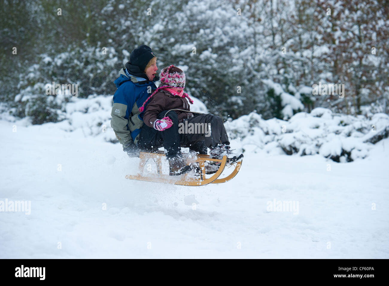 Mother and daughter having fun in the snow on a traditional wooden sled. Stock Photo