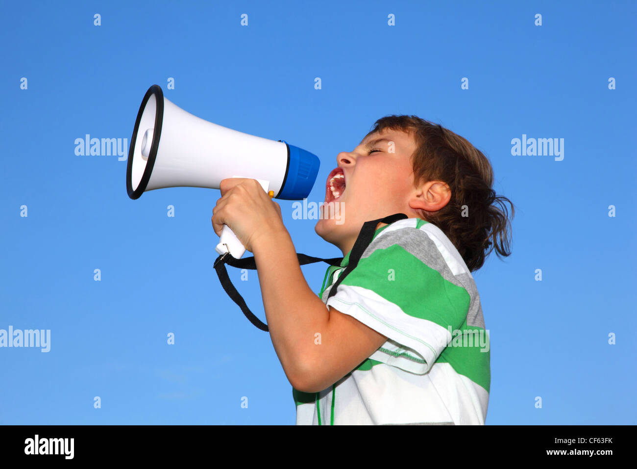 The small beautiful boy, against the blue sky, shouts in a loudspeaker. Profile side. Stock Photo