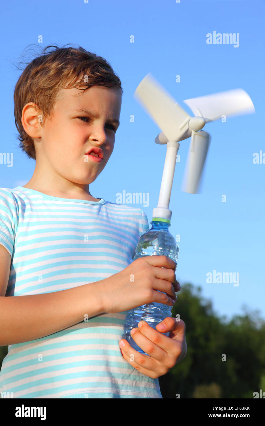 The little boy against the blue sky plays with a wind-driven generator. Stock Photo