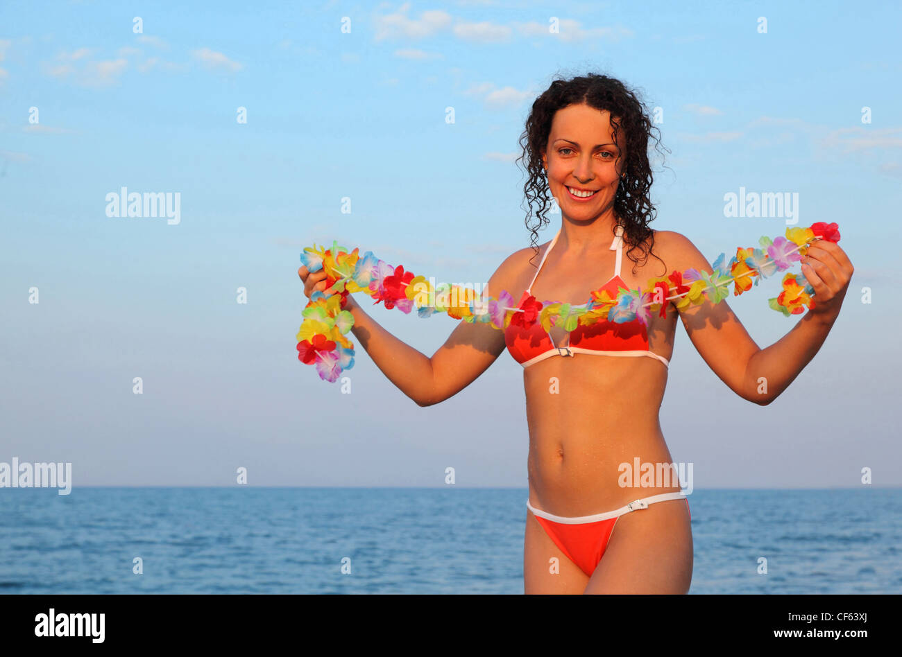 beautiful young woman dressed in bathing suit holding garland of hawaiian flower and stands on beach Stock Photo