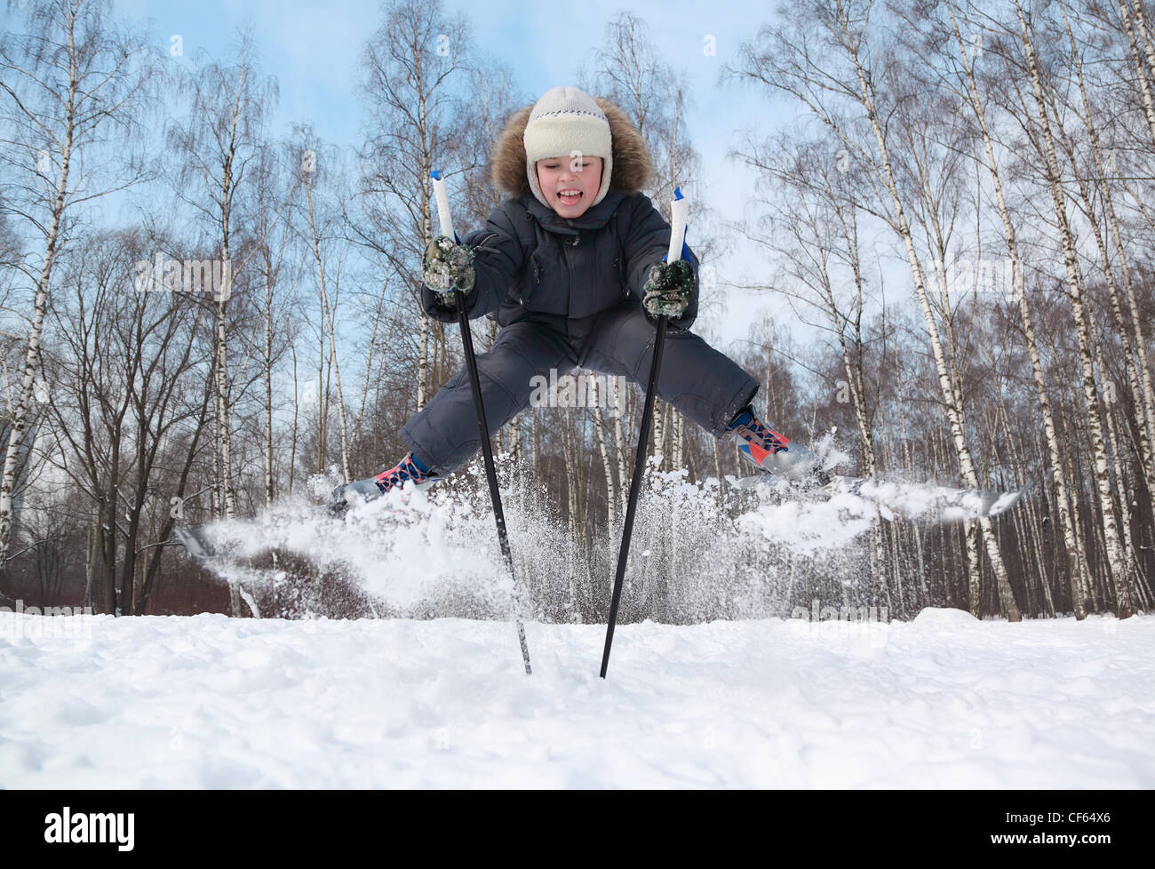 Young boy with crosscountry skis and poles jumps and tongue out inside