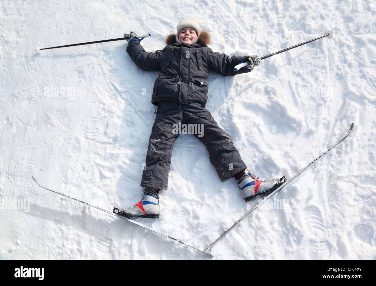 Young boy lying in crosscountry skis and poles and stretching out arms
