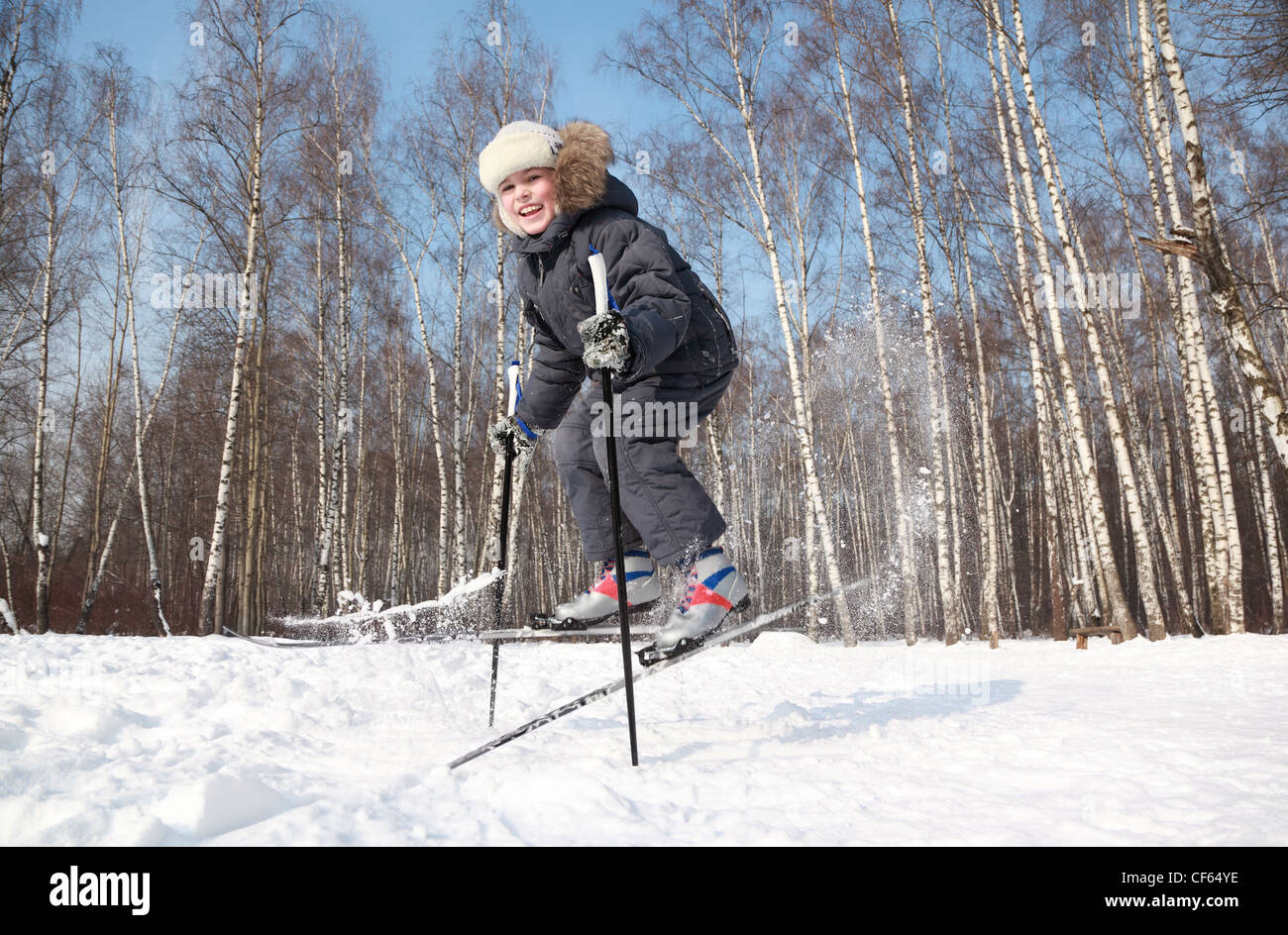 Young boy jumps sideways with crosscountry skis and poles inside