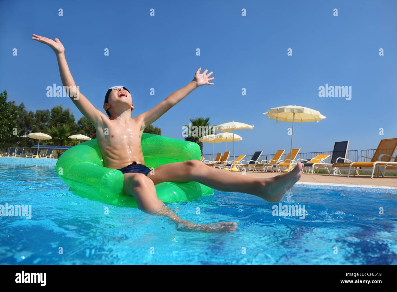 Boy sits on an inflatable arm-chair in  pool and with gladness lifts hands and head upwards in sky, underwater package shot Stock Photo