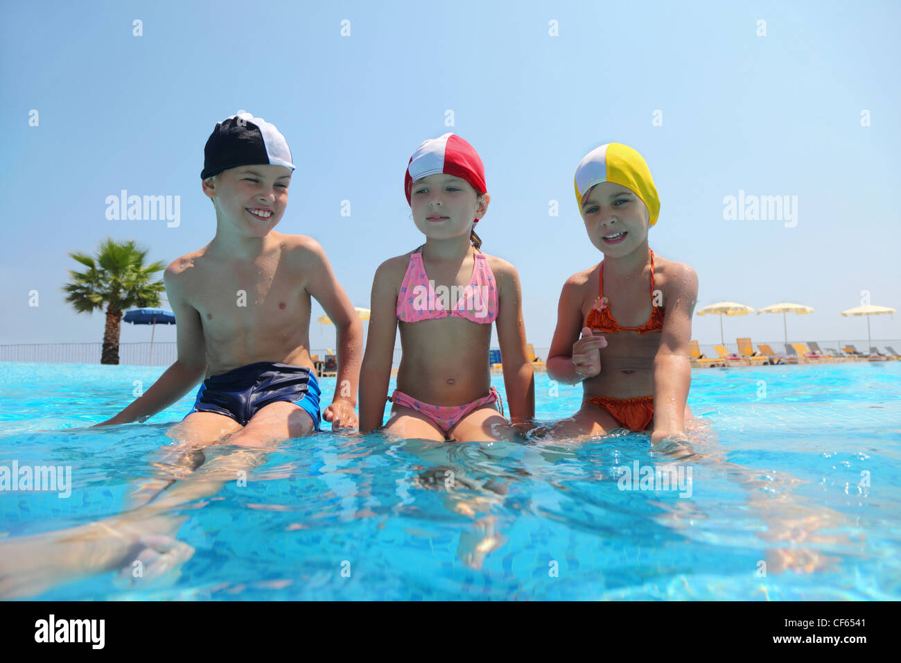 Two girls and boy sit on skirting in pool and speak, underwater package