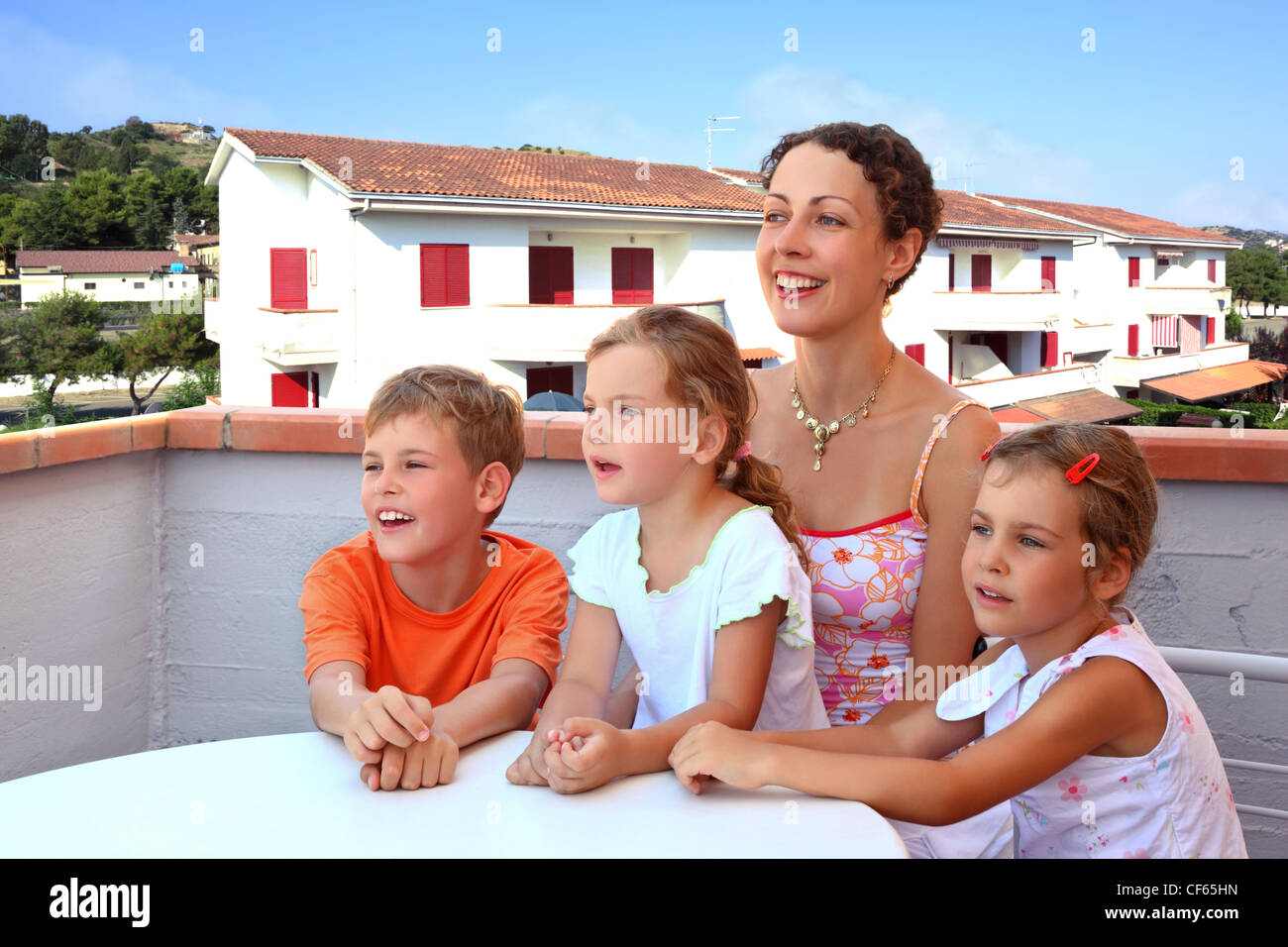 Mother and three children sit in  day-time on  balcony near  table and laugh Stock Photo