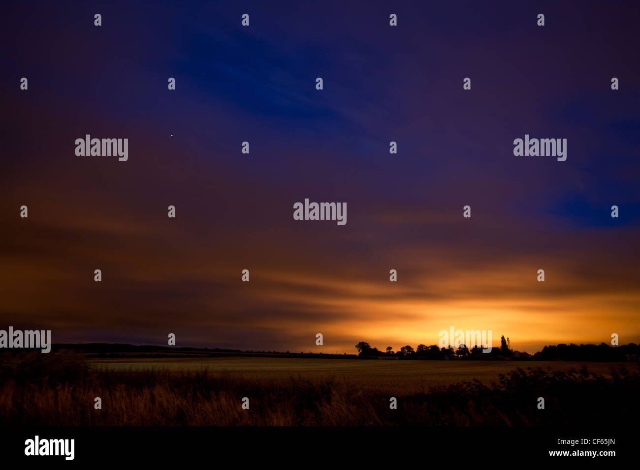 Twilight over a rural field, with distant streetlights reflecting off low clouds. Stock Photo