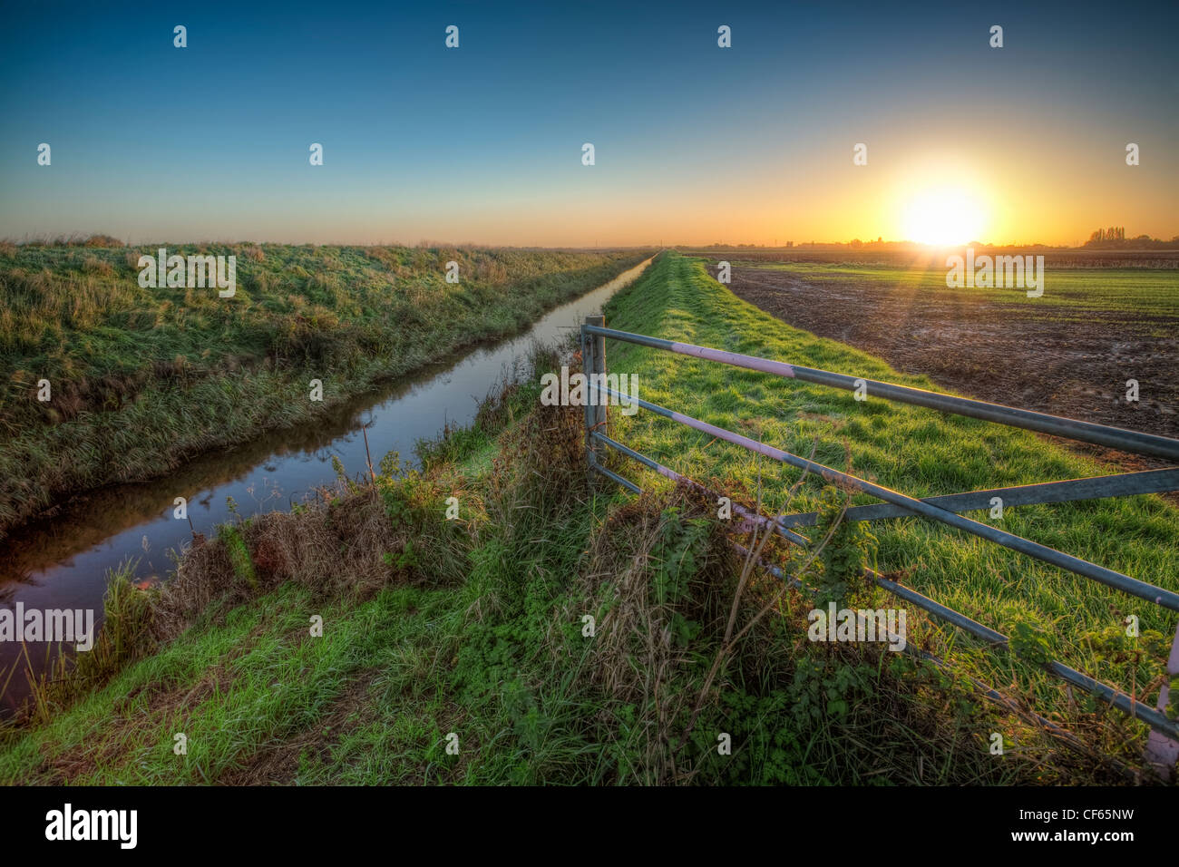 Sunrise over the Cambridgeshire Fens with a gate and stream between fields. Stock Photo