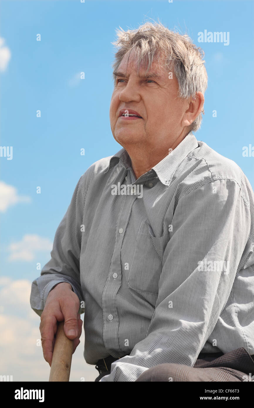 old senior in striped shirt with shovel digging, blue sky with clouds Stock Photo