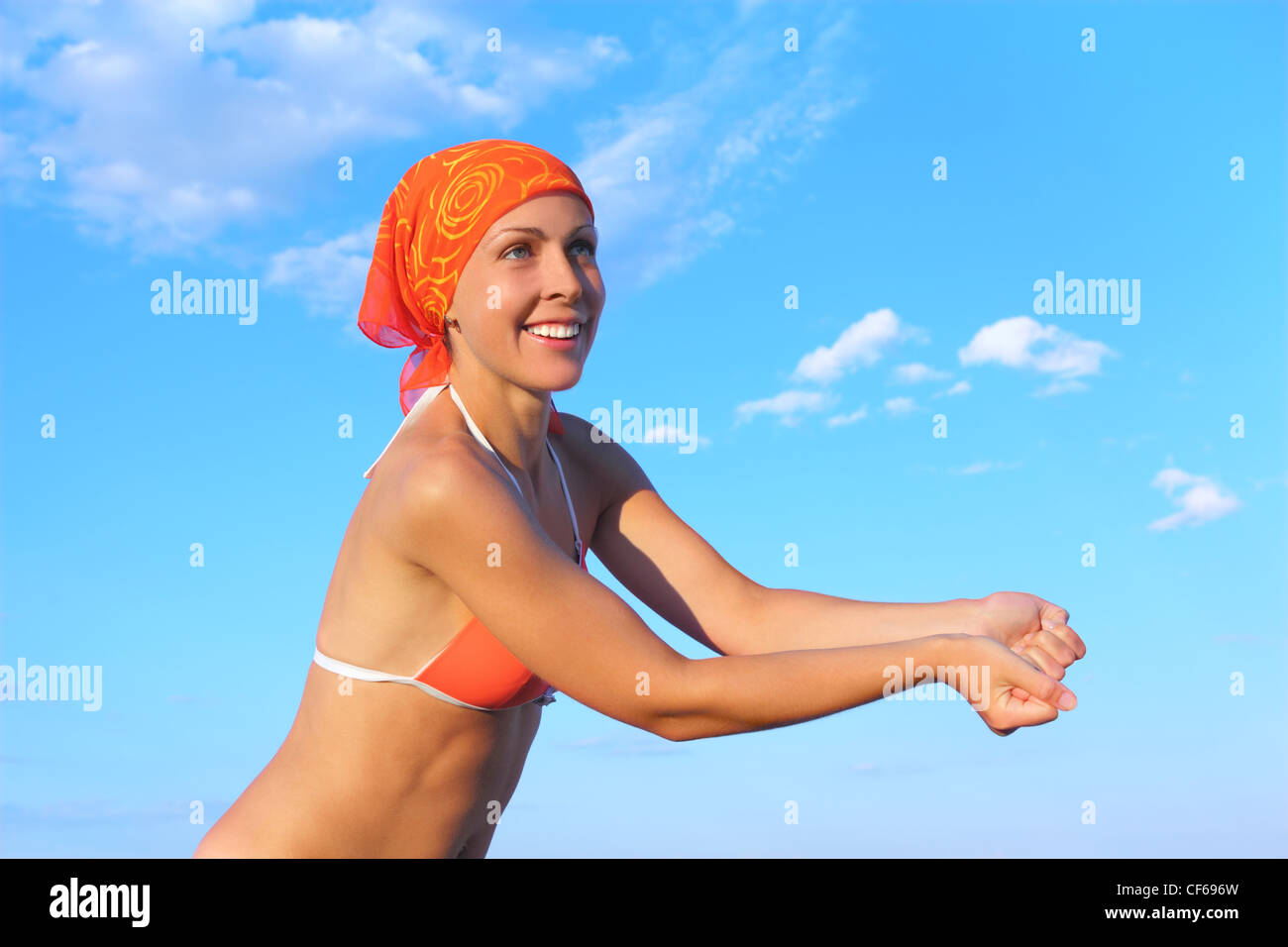 beauty woman in orange bikini and bandana playing volleyball, beat pose, blue sky Stock Photo